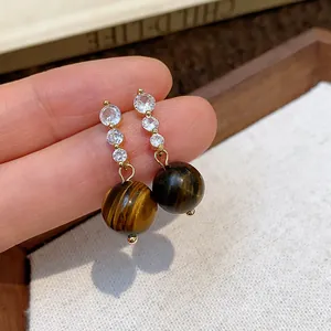 Dettaglio di eleganti orecchini a goccia in occhio di tigre con zirconi scintillanti