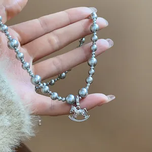 Close-up of elegant silver beaded necklace with textured rocking horse pendant held by hand