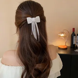 Elegant sparkling rhinestone bow hair clip with long tassels worn on wavy brown hair.