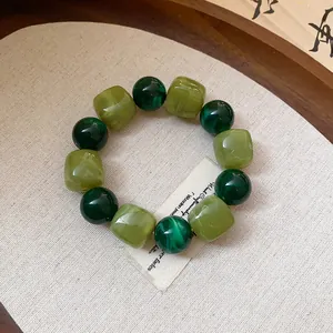 Close-up view of a green acrylic beaded bracelet with round and cube geometric bead shapes