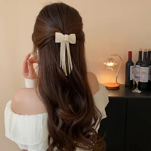 Elegant rhinestone bow hair clip with long tassels worn on wavy brown hair