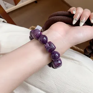 Macro detail view of a purple acrylic geometric beaded bracelet worn on a female wrist