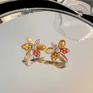 Elegant crystal flower stud earrings with colorful beads on a reflective mirror surface.