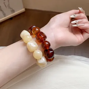Detailed macro shot of irregular amber and cream acrylic beaded bracelets on a woman's wrist