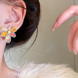 Close-up view of colorful crystal flower stud earrings with silver needles worn on ear
