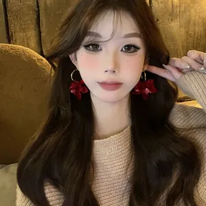 Elegante rote Kunstharz-Blumenohrringe getragen von einem Modell in gemütlicher Umgebung
