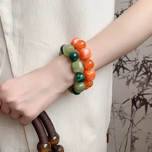 Close-up of acrylic irregular geometric beaded bracelets in green and orange tones on wrist.