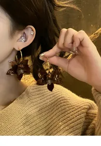 Nahaufnahme von braunen Kunstharz-Blumenohrringen mit goldenen Reifen an einem Model.