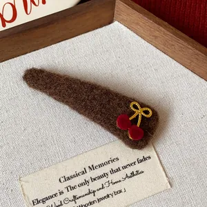 Detailed view of a brown plush triangular hair clip with a cute red cherry decoration.