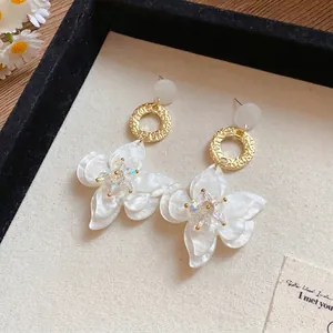 Elegant white resin flower dangle earrings with textured gold hoops in a display tray