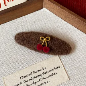 Close-up of a brown fuzzy hair clip with a gold bow and red cherries on white fabric