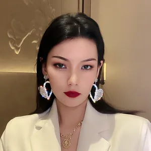 Close-up detail of oversized sparkling heart-shaped rhinestone earrings worn by a model