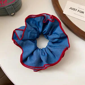 Detailansicht eines blauen Denim-Haargummis mit rotem Wellenrand und Paspelierung