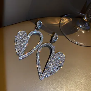 Close-up of oversized silver needle earrings with shimmering full rhinestone heart design