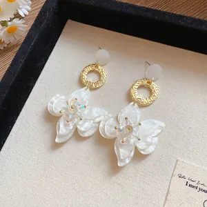 Close-up of white resin flower earrings with gold rings and iridescent crystals
