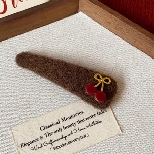 Detailed view of brown plush hair clip featuring red cherry and gold bow decorations
