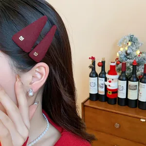 Close-up of a burgundy plush triangle hair clip with a gold B letter on an Asian model