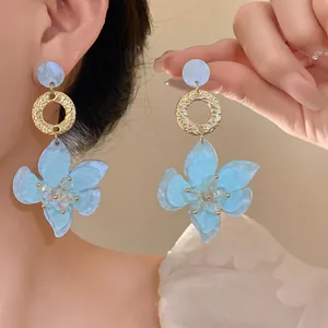 Detail of blue resin flower drop earrings with gold textured rings on model
