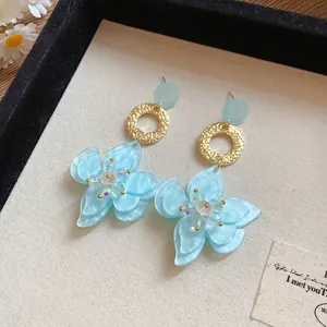 Detail view of light blue resin flower earrings with gold textured rings