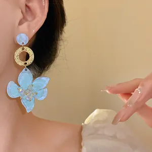 Detail of elegant blue resin flower pendant earrings with gold rings worn by model