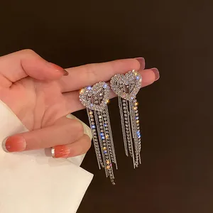 Close-up of elegant silver heart earrings with long sparkling rhinestone tassels.