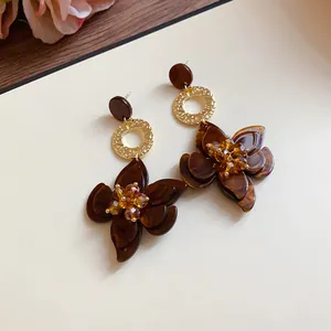 Detail of brown resin flower drop earrings with golden rings and crystal centers