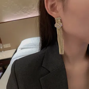 Elegant gold-tone heart-shaped rhinestone tassel earrings worn by a model in a close-up view.