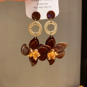 Close-up of brown resin flower drop earrings with 925 silver needles and gold accents.
