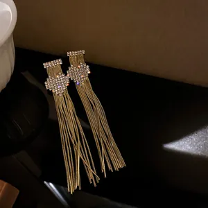 Detail view of elegant long golden tassel earrings with sparkling rhinestone bow accents