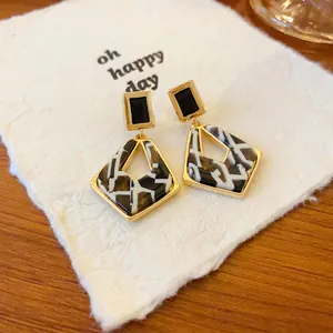 Close-up detail of geometric hollow earrings featuring black and white marble pattern