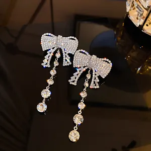 Close-up of silver bow tassel earrings with sparkling crystals on glossy black surface.