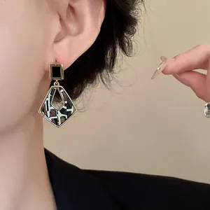 Close-up view of a chic geometric hollow earring featuring black and white patterned inlay