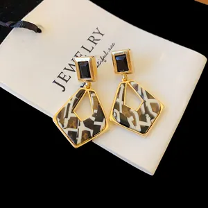 Close-up of geometric hollow earrings with gold plating, black stone and marble pattern