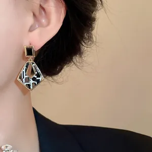 Close-up of geometric hollow drop earrings with black square and patterned diamond pendant