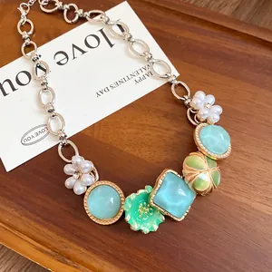 Detail of a bohemian necklace with pearl flowers and teal charms on a wooden tray