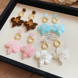 Detailed view of four pairs of resin flower pendant earrings in brown, pink, blue and white