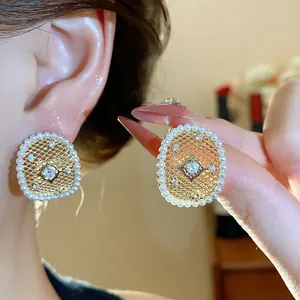 Dettaglio di orecchini a maglia placcati oro 18k con bordi di perle e zircone centrale.