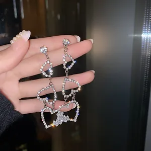 Sparkling heart-shaped silver dangling earrings with pavé-set rhinestones held by hand