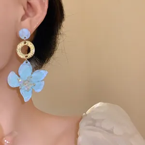 Close-up of elegant light blue resin flower drop earrings with gold ring worn by a model.
