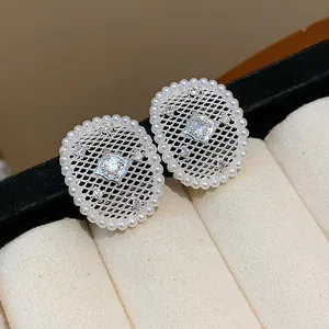 Dettaglio di eleganti orecchini a lobo in maglia d'argento con perle e zircone centrale