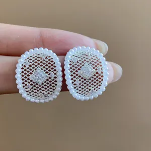 Primo piano di eleganti orecchini in maglia d'argento con perle e zircone centrale