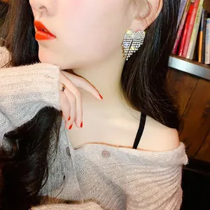 Elegant full rhinestone heart tassel earrings worn by a model in a cozy indoor setting.