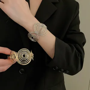 Close-up of elegant gold and silver spiral open cuff bracelets worn with a black blazer.