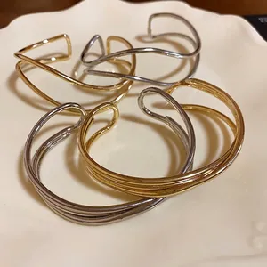 Bracciali a fascia aperti incrociati multistrato in oro e argento su piatto decorativo.