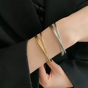 Dettaglio di eleganti bracciali a polsino incrociati multistrato in oro e argento su polso.