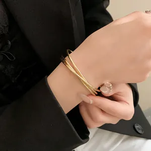 Dettaglio ravvicinato di un bracciale rigido a strati incrociati in oro minimalista