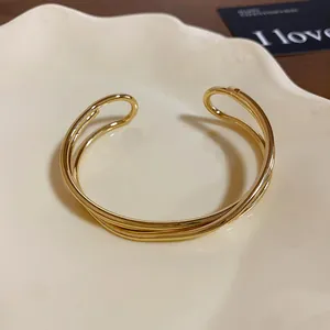 Dettaglio del bracciale rigido aperto multistrato dorato minimalista con finitura lucida.