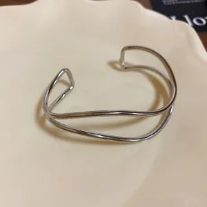 Dettaglio di un bracciale rigido aperto in metallo argentato multistrato dallo stile minimalista