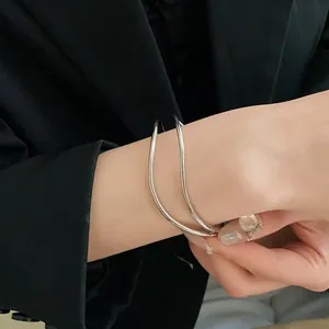 Vista dettagliata di un bracciale rigido aperto multistrato incrociato argento minimalista.