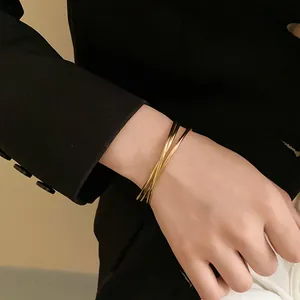 Primo piano di un bracciale rigido dorato minimalista a più strati indossato sul polso.